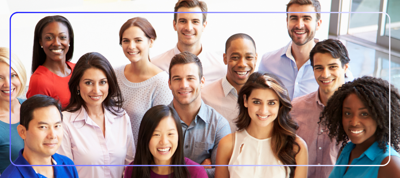 Group of teachers stand together smiling and looking at the camera. There is a mix of male, female, diverse races, and ages.