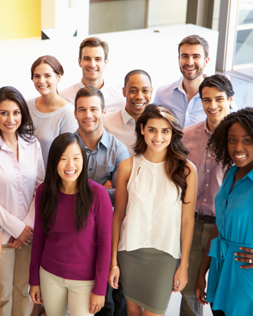 Group of teachers stand together smiling and looking at the camera. There is a mix of male, female, diverse races, and ages.
