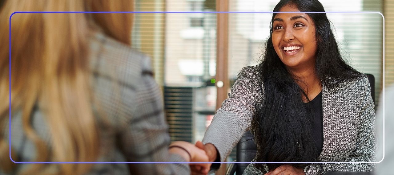 Smiling candidate shaking hands with an interviewer across a desk in a modern office, representing a successful teaching interview.